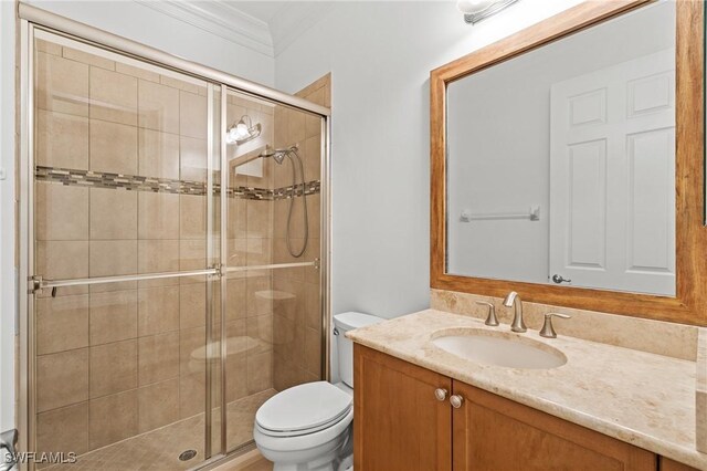 bathroom featuring vanity, a shower with shower door, ornamental molding, and toilet