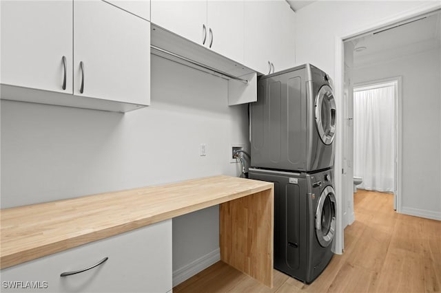 laundry room with stacked washer and dryer, light wood-style flooring, cabinet space, and baseboards