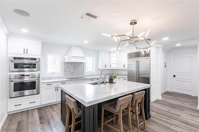 kitchen featuring sink, custom exhaust hood, a center island with sink, appliances with stainless steel finishes, and pendant lighting