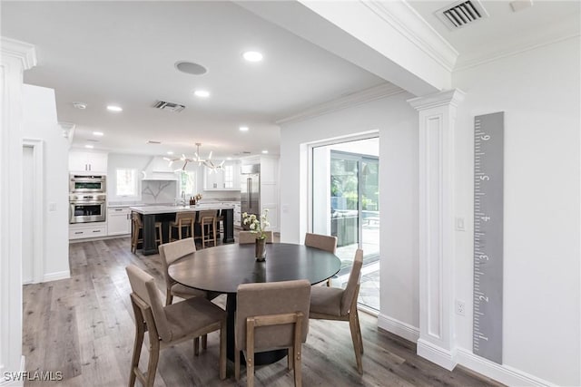 dining space featuring hardwood / wood-style flooring, ornamental molding, an inviting chandelier, and ornate columns