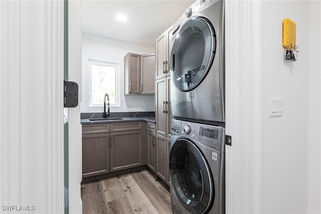 washroom featuring sink, cabinets, ornamental molding, stacked washer / drying machine, and light hardwood / wood-style floors