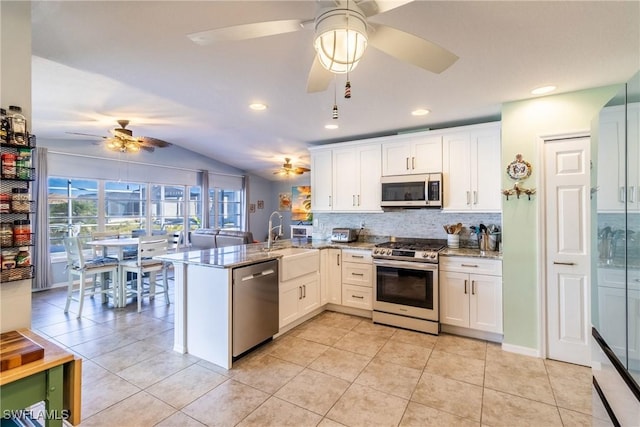 kitchen featuring kitchen peninsula, stainless steel appliances, vaulted ceiling, white cabinets, and sink