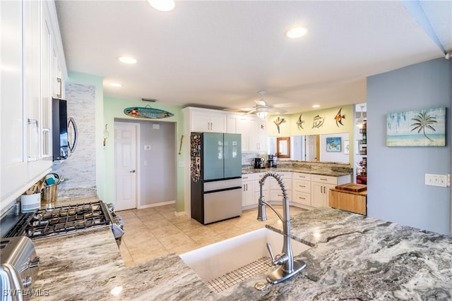 kitchen featuring light stone countertops, white cabinetry, sink, kitchen peninsula, and refrigerator