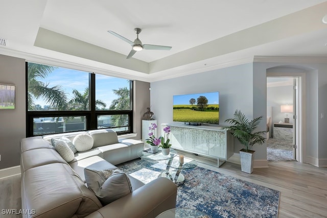 living room featuring a ceiling fan, a tray ceiling, wood finished floors, and baseboards