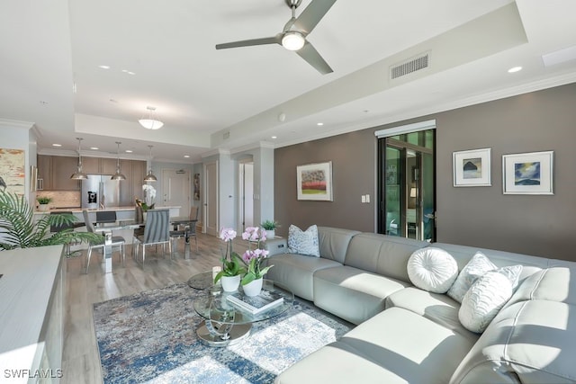 living room with a tray ceiling, light wood finished floors, a ceiling fan, recessed lighting, and crown molding