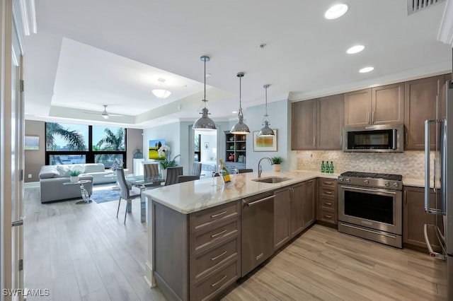 kitchen with stainless steel appliances, a sink, a peninsula, backsplash, and a raised ceiling
