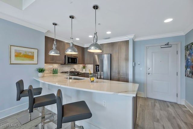 kitchen featuring crown molding, a breakfast bar area, stainless steel appliances, a sink, and a peninsula