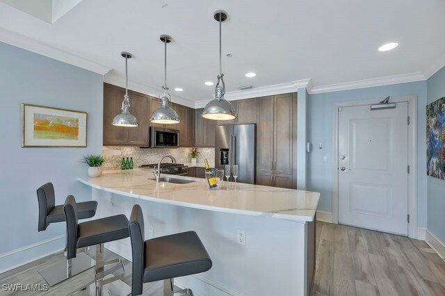 kitchen with ornamental molding, a kitchen breakfast bar, appliances with stainless steel finishes, a peninsula, and a sink