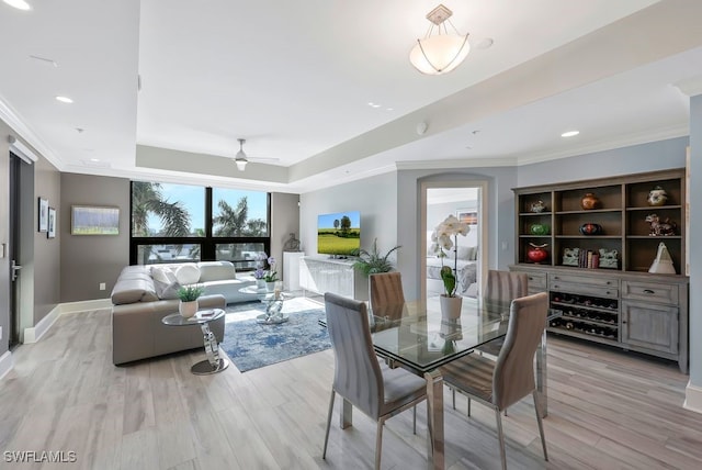 dining space with a raised ceiling, light wood-type flooring, ceiling fan, ornamental molding, and baseboards