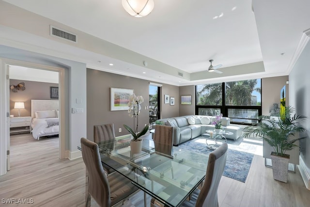 dining space with a raised ceiling, light wood-style flooring, crown molding, baseboards, and ceiling fan