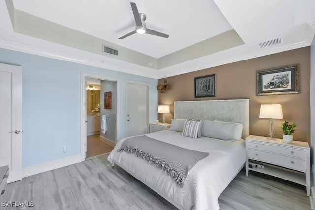 bedroom with a tray ceiling, light wood finished floors, baseboards, and connected bathroom