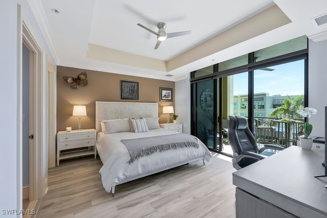 bedroom featuring light wood-style flooring, ceiling fan, access to exterior, expansive windows, and a raised ceiling