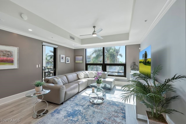 living room featuring a tray ceiling, light wood-type flooring, plenty of natural light, crown molding, and a ceiling fan