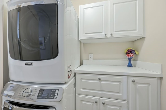 clothes washing area with stacked washing maching and dryer and cabinet space