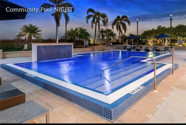 pool at dusk with a patio and a community pool