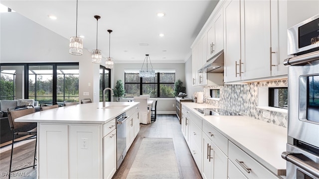 kitchen with sink, decorative light fixtures, white cabinetry, and a center island with sink