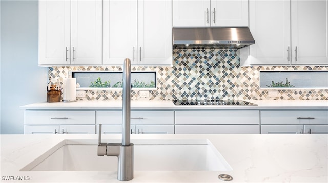 kitchen featuring black electric cooktop, white cabinets, range hood, and light stone countertops