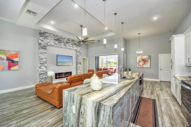 kitchen with hanging light fixtures, light stone counters, a large fireplace, white cabinets, and a large island with sink