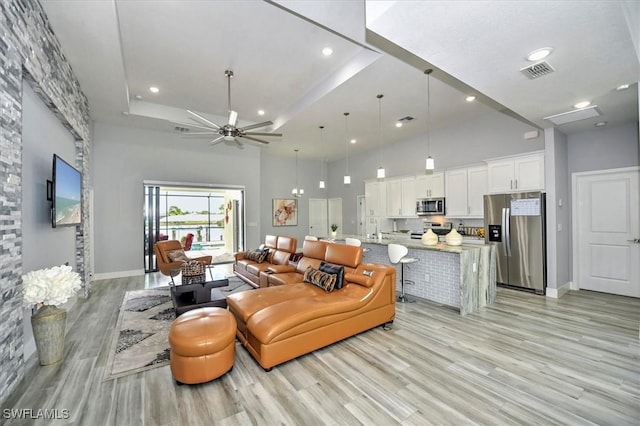 living room featuring a high ceiling, ceiling fan, light hardwood / wood-style floors, and a tray ceiling