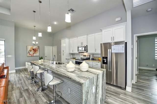 kitchen with decorative light fixtures, a large island with sink, appliances with stainless steel finishes, white cabinets, and a high ceiling