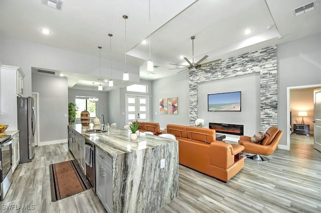 kitchen featuring decorative light fixtures, an island with sink, a large fireplace, white cabinets, and light stone countertops