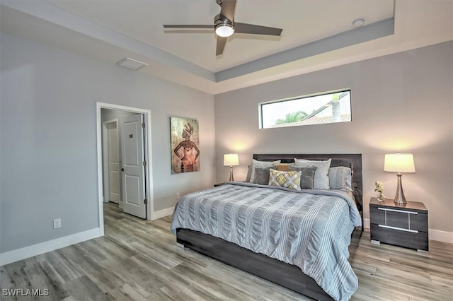 bedroom featuring ceiling fan, a raised ceiling, and light wood-type flooring