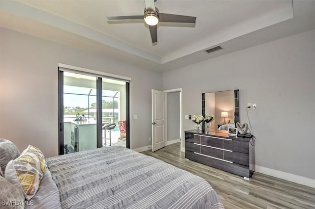 bedroom featuring ceiling fan, a tray ceiling, light hardwood / wood-style floors, and access to outside