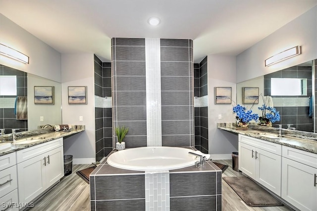 bathroom with hardwood / wood-style flooring, vanity, and a relaxing tiled tub