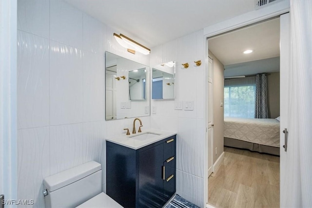 bathroom featuring tile walls, toilet, connected bathroom, vanity, and wood finished floors