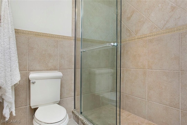 bathroom with toilet, a shower with shower door, and tile walls