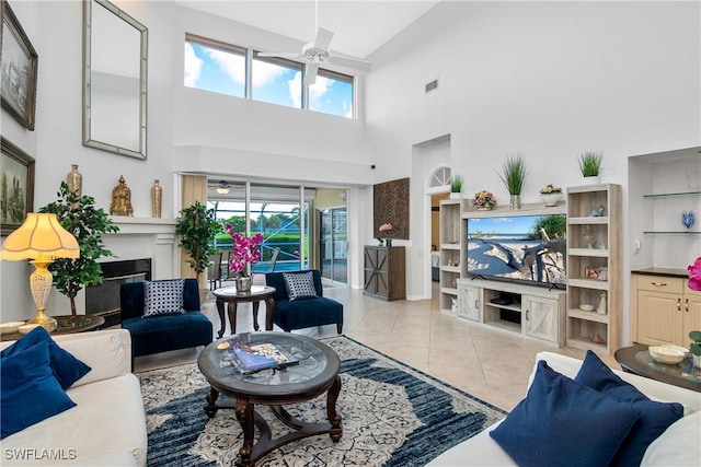 tiled living room with built in shelves, ceiling fan, a wealth of natural light, and a towering ceiling