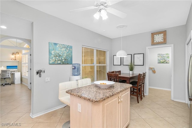 kitchen with light tile patterned floors, ceiling fan, a kitchen island, decorative light fixtures, and light brown cabinets