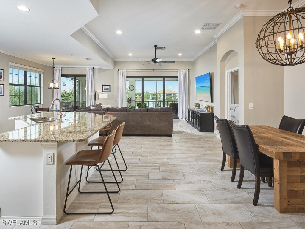 kitchen with a breakfast bar, pendant lighting, a kitchen island with sink, a sink, and light stone countertops