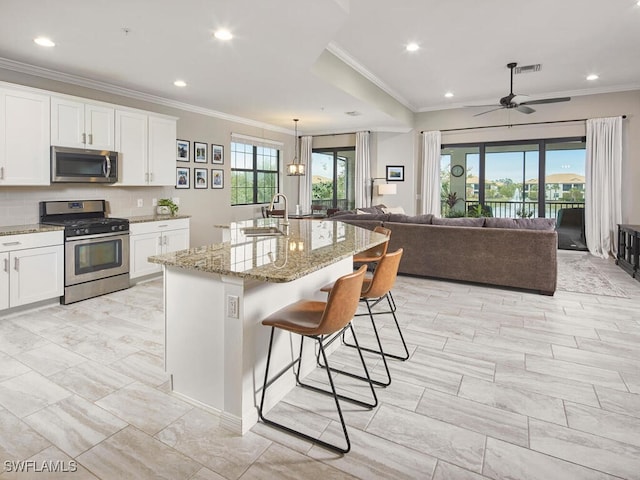 kitchen featuring light stone countertops, appliances with stainless steel finishes, white cabinets, a breakfast bar, and an island with sink