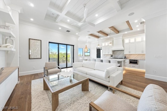 living room featuring beamed ceiling, ceiling fan, ornamental molding, hardwood / wood-style flooring, and coffered ceiling