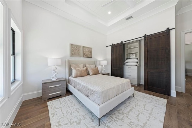 bedroom featuring a towering ceiling, crown molding, a barn door, and light wood-type flooring