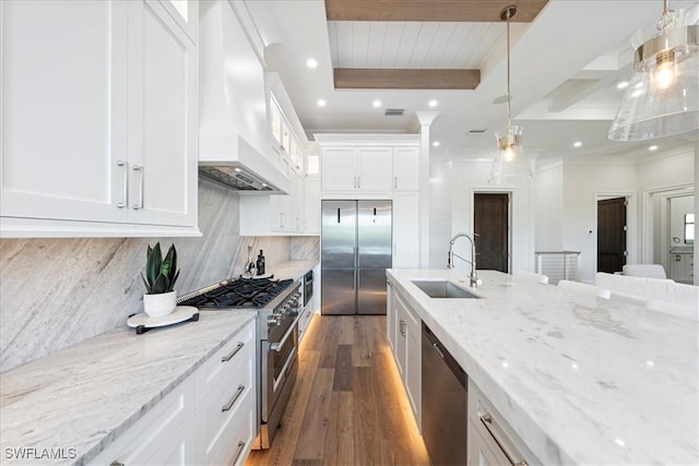 kitchen featuring custom exhaust hood, white cabinetry, high end appliances, sink, and hanging light fixtures