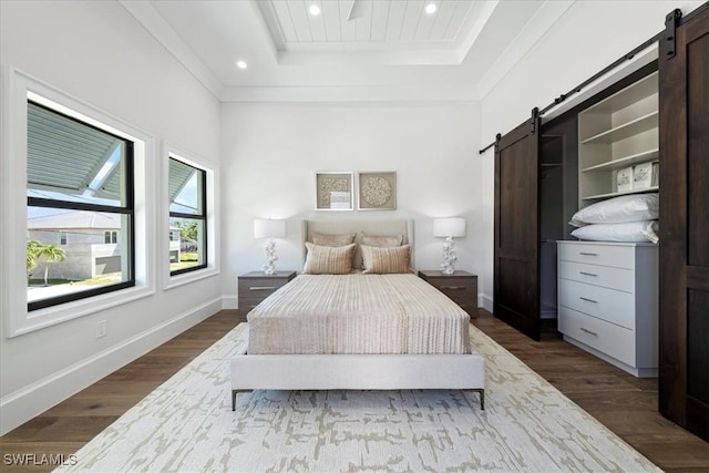 bedroom featuring wood-type flooring, ornamental molding, a raised ceiling, and a barn door