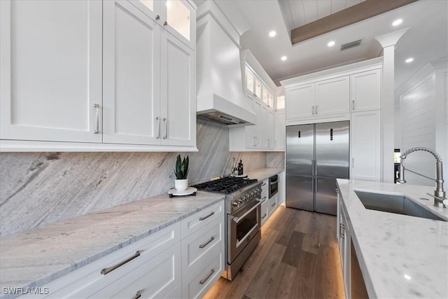 kitchen featuring custom exhaust hood, sink, white cabinetry, light stone counters, and high end appliances