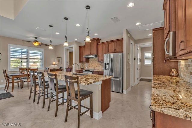 kitchen with decorative backsplash, sink, stainless steel appliances, light stone counters, and a center island with sink