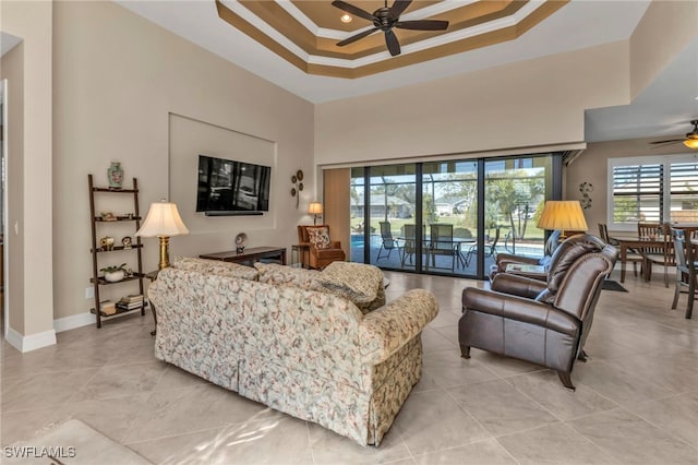 living room featuring ceiling fan, a raised ceiling, ornamental molding, and a towering ceiling