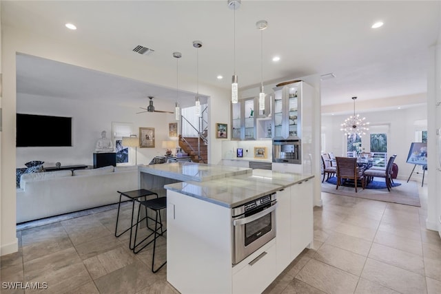 kitchen featuring a spacious island, decorative light fixtures, white cabinetry, a kitchen bar, and stainless steel oven