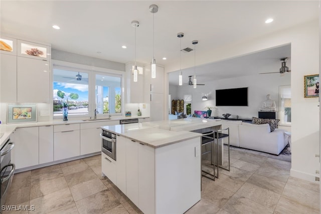 kitchen featuring hanging light fixtures, appliances with stainless steel finishes, sink, white cabinetry, and a center island