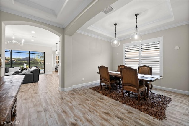 dining space with a raised ceiling, light wood finished floors, arched walkways, and a notable chandelier