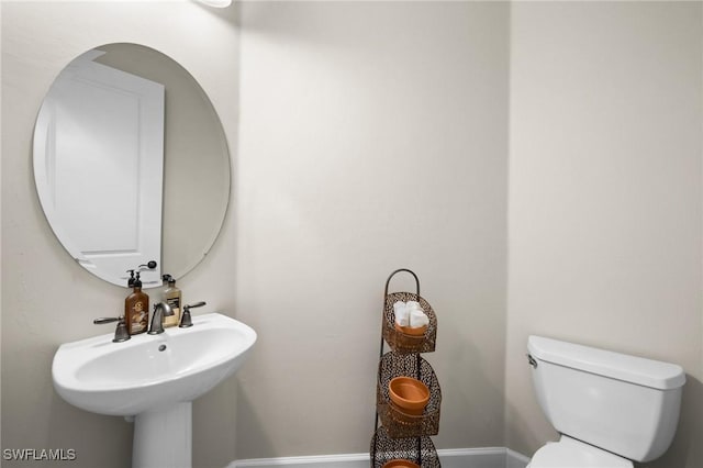 bathroom featuring toilet, baseboards, and a sink