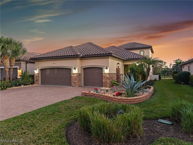 mediterranean / spanish-style house featuring an attached garage, stone siding, stucco siding, decorative driveway, and a lawn