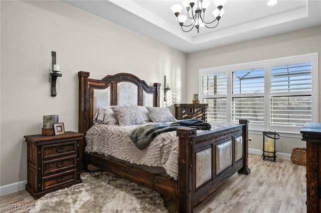 bedroom featuring baseboards, a notable chandelier, light wood-style flooring, and a raised ceiling