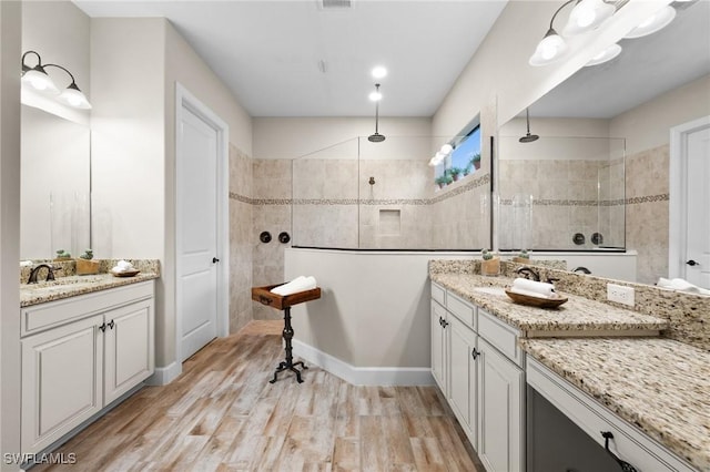 full bath featuring a sink, walk in shower, wood finished floors, and two vanities