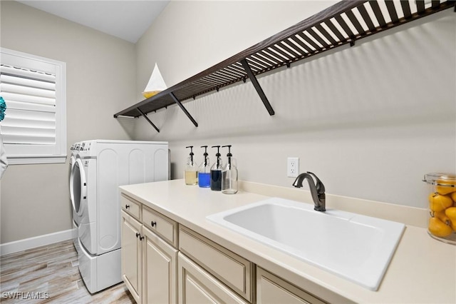 laundry room with cabinet space, a sink, light wood finished floors, baseboards, and washing machine and dryer