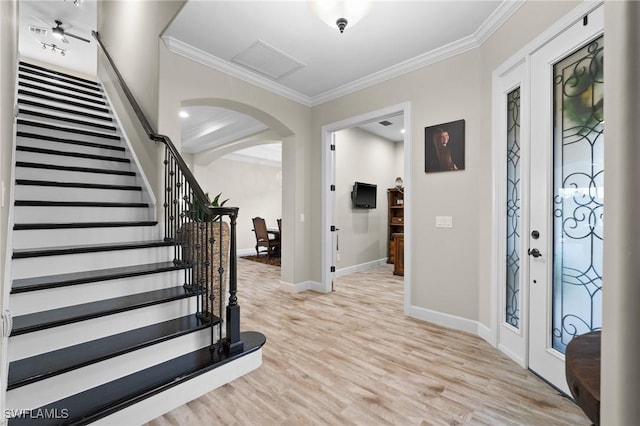 entryway featuring light wood finished floors, arched walkways, baseboards, ornamental molding, and stairway